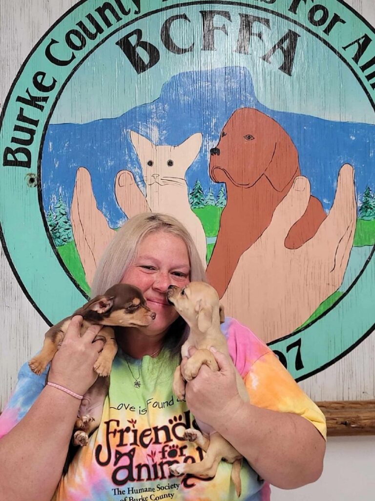 A woman in a Friends for Animals shirt holding two puppies